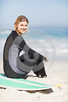 Portrait of woman in wetsuit sitting with surfboard on the beach