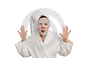 A portrait of a woman in a white bathrobe and a towel on her head with a moisturizing mask on her face