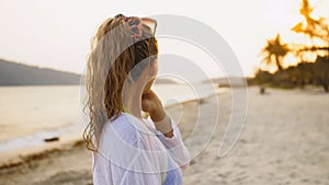 Portrait woman in a white tunic shirt on beach, near stormy sea. Girl in sunglasses. Female tourist walks. Rear view