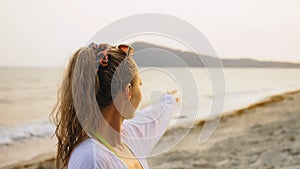Portrait woman in a white tunic shirt on beach, near stormy sea. Girl in sunglasses. Female tourist walks. Rear view