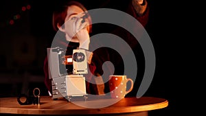 Portrait of woman who sits at the table where there is a slide projector and watches photo negatives