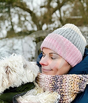 Portrait of a woman in winter clothes with her puppy dog. Happy woman and little maltese pet together.
