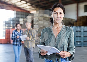 Portrait of woman worker standing with papers near crates with peaches in warehouse