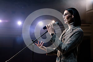 Portrait of women speaking through a microphone in dark conference hall. woman talks into microphones at press