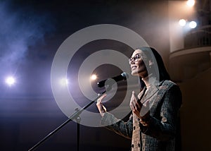 Portrait of women speaking through a microphone in dark conference hall. woman talks into microphones at press