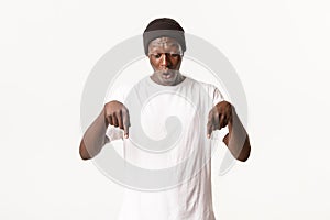 Portrait of wondered and amazed african-american guy in beanie, handsome man pointing fingers down and looking surprised