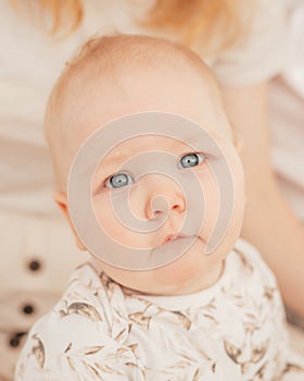 Portrait of wonderful serious grey-eyed plump cherubic baby infant toddler wearing beige bodysuit with patterns sitting. photo