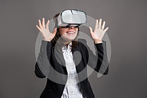 Portrait of wonderful young business woman wearing virtual reality VR glasses, poseing on isolated gray background