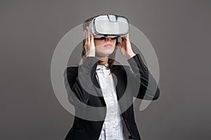 Portrait of wonderful young business woman wearing virtual reality VR glasses, poseing on isolated gray background