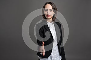 Portrait of wonderful young business woman shakeing hand, poseing on isolated gray background