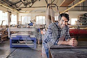 Woodworker smiling while leaning on a bench in his workshop photo