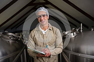 Portrait of worker amidst storage tanks writing on clipboard