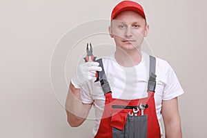 Portrait of a worker in red uniform, cap and white glove holding pliers, isolated on white background. Work concept