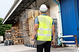 Portrait of worker working in logistic industry outdoor in front of factory warehouse. Man with hard hat looking at