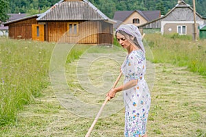 Portrait of a working woman. She turns hay with a wooden rake