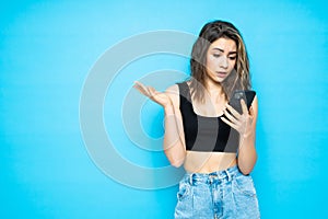 Portrait of a worried confused girl with mobile phone isolated over blue background