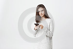 Portrait of worried and frustrated cute european student, holding smartphone and wearing earphones, over white