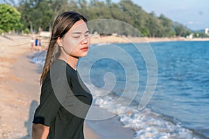 Portrait of a worried girl standing on the beach with green nature and blue sea in the background. Sad and depressed young woman