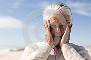 Portrait of worried senior biracial woman with hands covering face at beach on sunny day