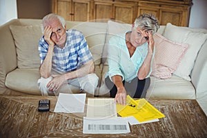 Portrait of worried senior couple checking bills in living room