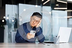 Portrait of a worried young Asian man looking sadly at the phone. Bored, received bad news
