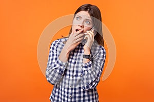 Portrait of worried young woman with brown hair talking on phone. isolated on orange background