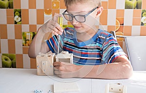 Portrait of a 7-8 year old boy with a screwdriver, carefully assembling a wooden car, sitting at the kitchen table