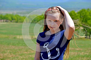 Portrait of 10 year old Russian blonde girl with long hair, hair band on a background of green field. cute face, looking at the ca