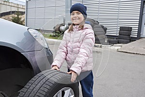 Portrait of a 6 years old girl with a car wheel in hands. Car service. Repair service