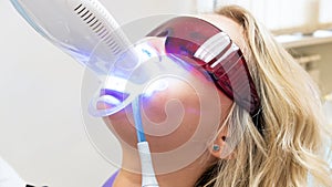 Closeup portrait of youn gblonde woman sitting in dentist chair during teeth whitening procedure with photopolymer photo