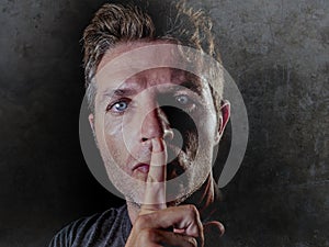 Portrait of young 30s man with finger on his lips in silence and shut up hand gesture warning or threatening not to speak in polit