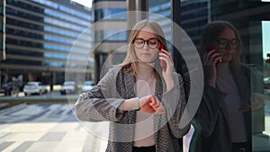 Portrait of a young 30s woman talking on the phone on a break and checking the time on her watch