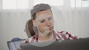 Portrait of young absorbed Caucasian man using laptop with blurred woman surfing Internet at the background. Millennial