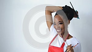 Portrait of the young adorable african make-up artist with pretty smile holding the set of brushes and palette over