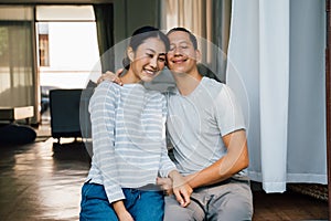 Portrait of young adult Asian couple embracing together with home interior in background. 30s happy mature husband and