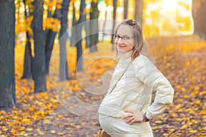 Portrait of young adult beautiful caucasian pregnant girl enjoy walking at scenic autumn city park. Happy woman smiling