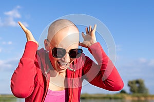 Portrait of young adult beautiful caucasian short haired bald woman in sunglasses shouting with hands raised up and