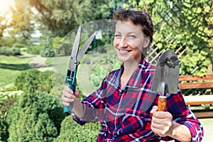 Portrait of young adult happy beautiful caucasian brunette woman grower worker holding shears and showel spade with green formal