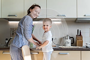 Portrait young adult mother learn cooking sweet tasty cookies cute little toodler boy kid at home kitchen. Mom with