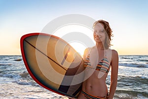 Portrait young adult slim sporty female surfer girl with surfboard silhouette stand at ocean coast wave against warm