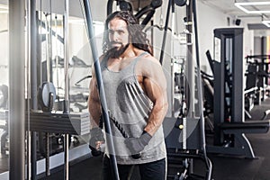 Portrait of young adult sport athlete man with long curly hair training at gym alone, standing and lifting weights in the gym,