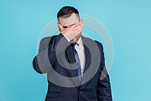 Portrait of young adult wearing official style suit closing eyes with hand, dont want to see that