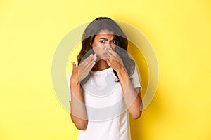 Portrait of young african-american girl, shut her nose and looking at something with disgusting smell, complaining on