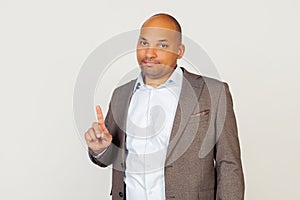 Portrait of a young African American guy businessman showing his forefinger asking to wait a minute. Standing on a gray background
