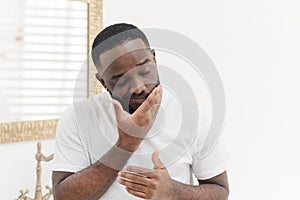 Portrait of young african american man applying nourishing face cream or balm in bathtub, skincare concept