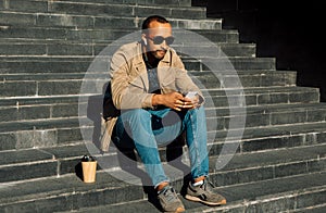 Portrait of young african american man sitting on steps using mobile