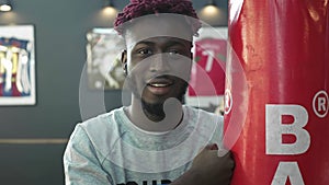 Portrait: a young African American is smiling at the camera, hugging a boxing bag