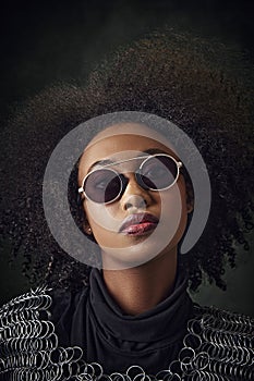 Portrait of young African-American woman with curly hair, wearing sunglasses and chainmail, standing against vintage