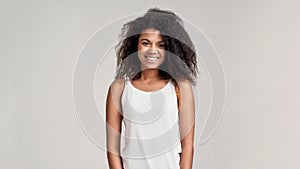 Portrait of young african american woman with curly hair wearing white shirt smiling at camera while standing isolated