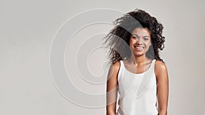 Portrait of young african american woman with curly hair wearing white shirt smiling at camera while standing isolated